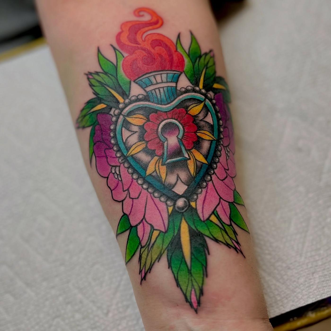 A neo-traditional heart-shaped locket wrapped in peonies with a flame above it, on a forearm.