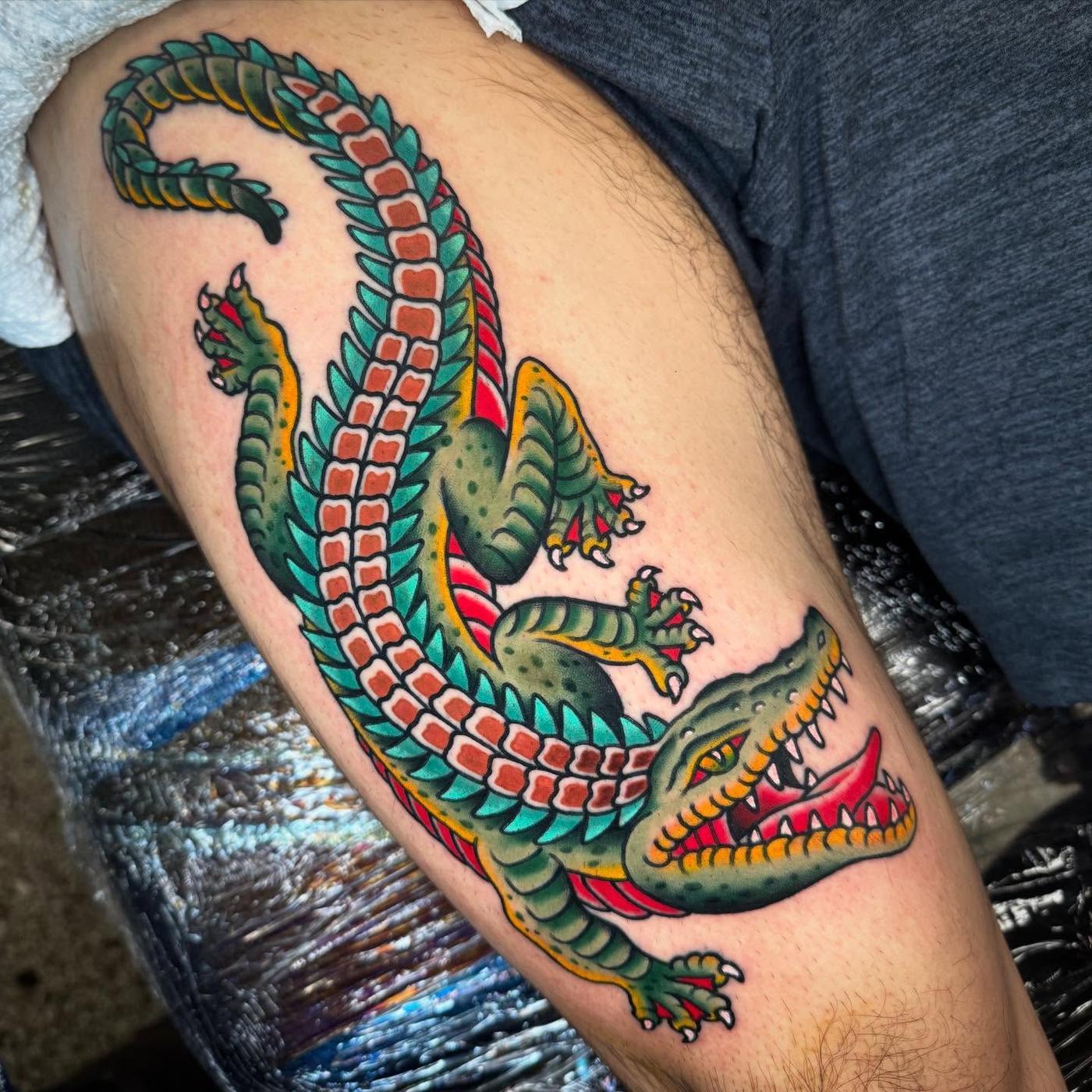 A traditional alligator in green, teal and red, running down a thigh.