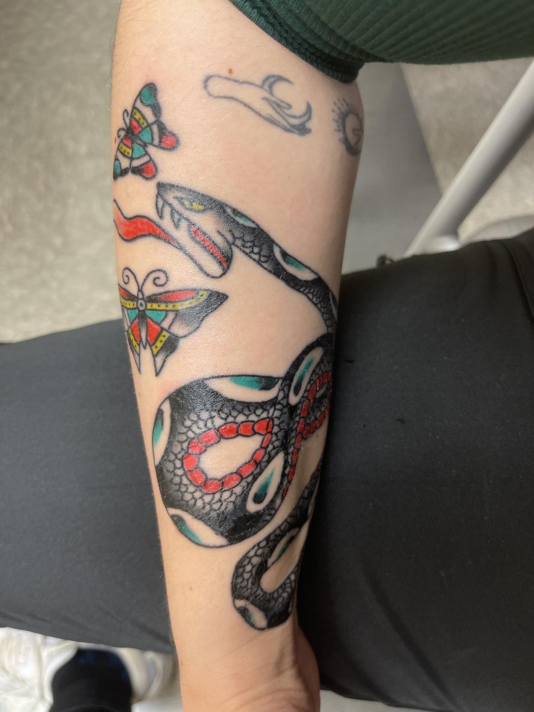 Traditional snake and butterflies in red, teal and black on a forearm.